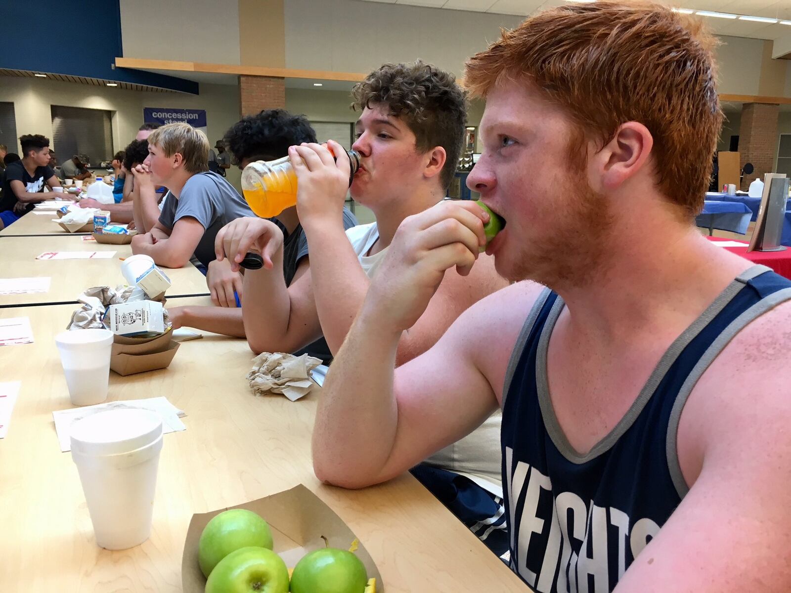 Members of Hamilton High School’s football squad are trying a new addition to their pre-season workouts. Besides learning their team’s plays and strategies, the teens are also learning about the importance of nutrition. Players pictured help themselves to healthy snacks while listening to a lecture by a nutritional expert. 