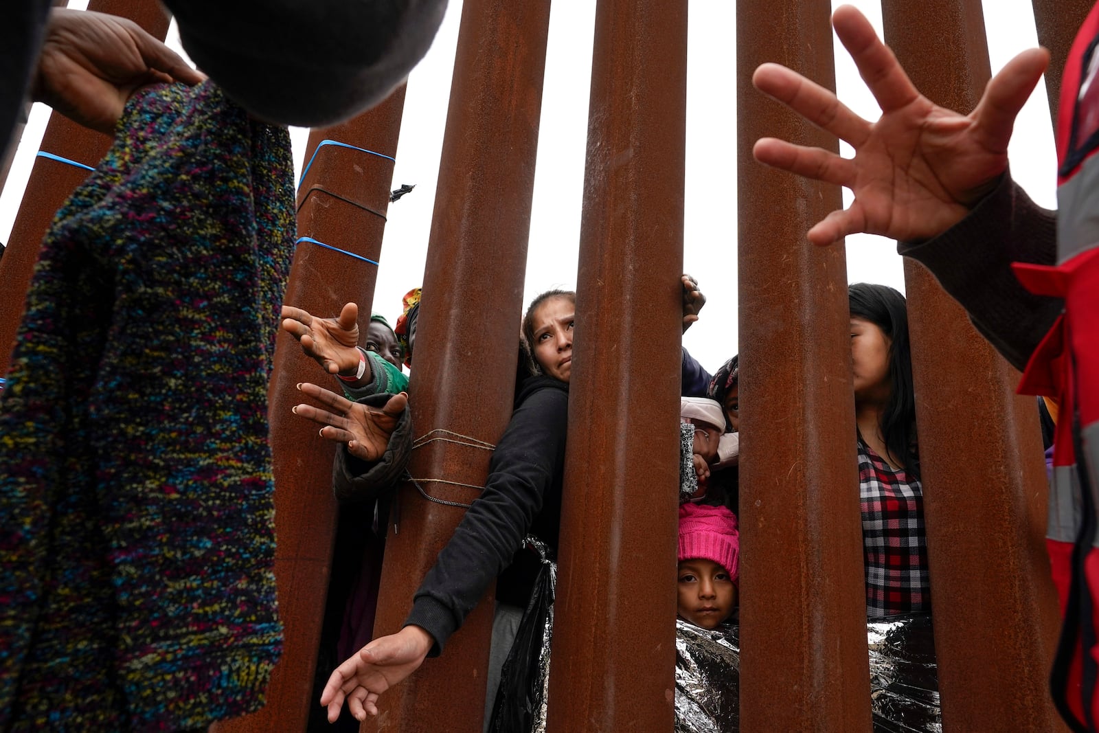 FILE - Migrants reach through a border wall for clothing handed out by volunteers as they wait for asylum, May 12, 2023, in San Diego, Texas. (AP Photo/Gregory Bull, File)