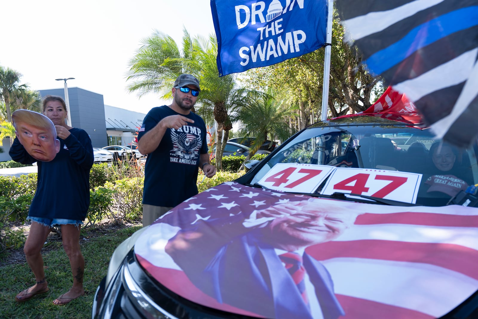 Supporters of President Donald Trump Jestin Nevarez, right, and Heather Dowling join a rally to support Elon Musk and the Department of Government Efficiency (DOGE) outside a Tesla car dealership, Saturday, April 12, 2025, in West Palm Beach, Fla. (AP Photo/Manuel Balce Ceneta)
