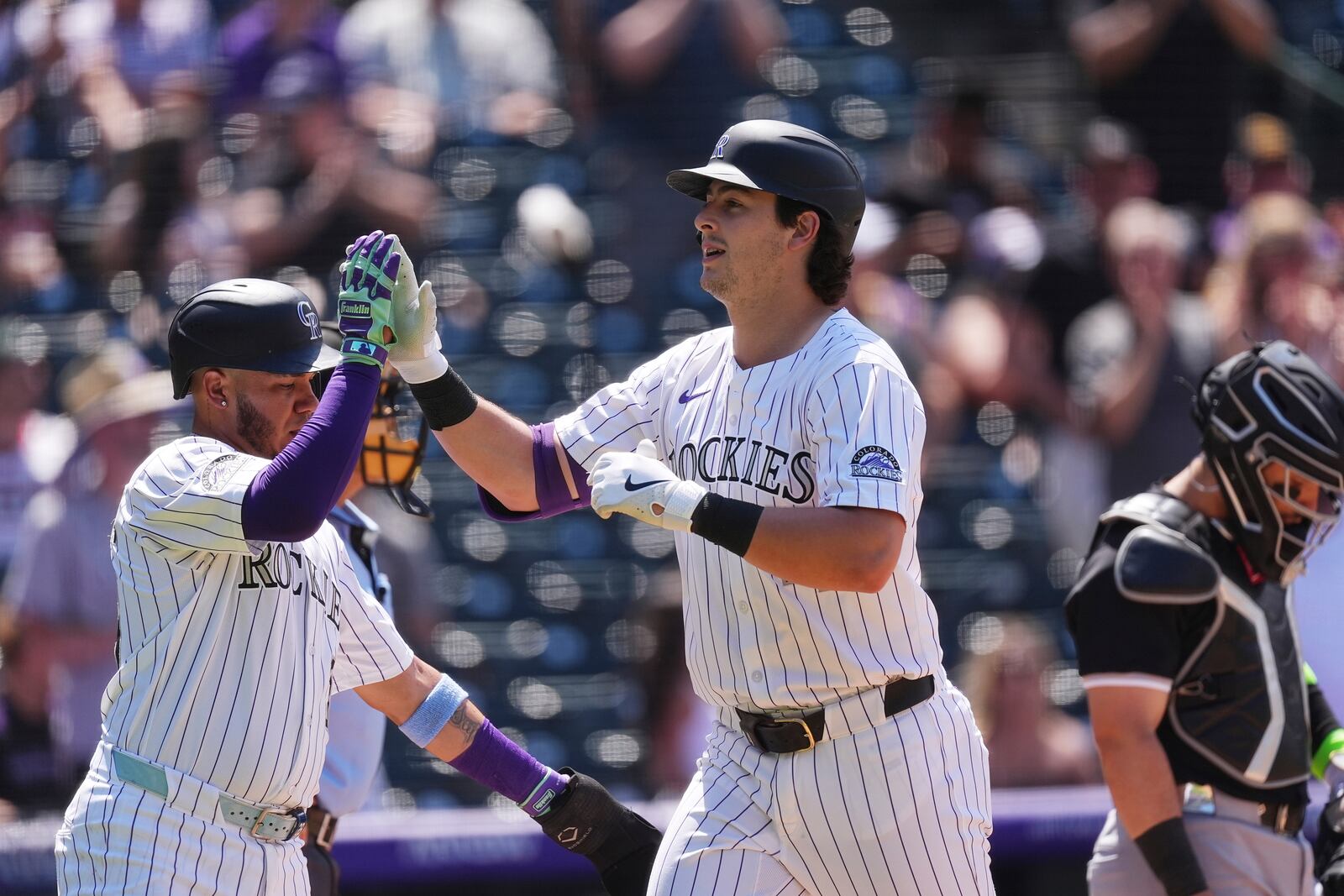 Colorado Rockies' Thairo Estrada, left, congratulates Michael Toglia, center, who crosses home plate after hitting a two-run home run off Chicago White Sox relief pitcher Dan Altavilla in the fifth inning of a baseball game Sunday, July 6, 2025, in Denver. (AP Photo/David Zalubowski)