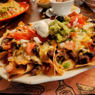 A heaping plate of corn tortilla chips piled high with melted cheese and assorted toppings. ISTOCK