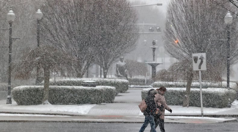The snow Friday, Feb. 16, 2024 partially obscures two people as they cross Fountain Avenue in downtown Springfield. BILL LACKEY/STAFF