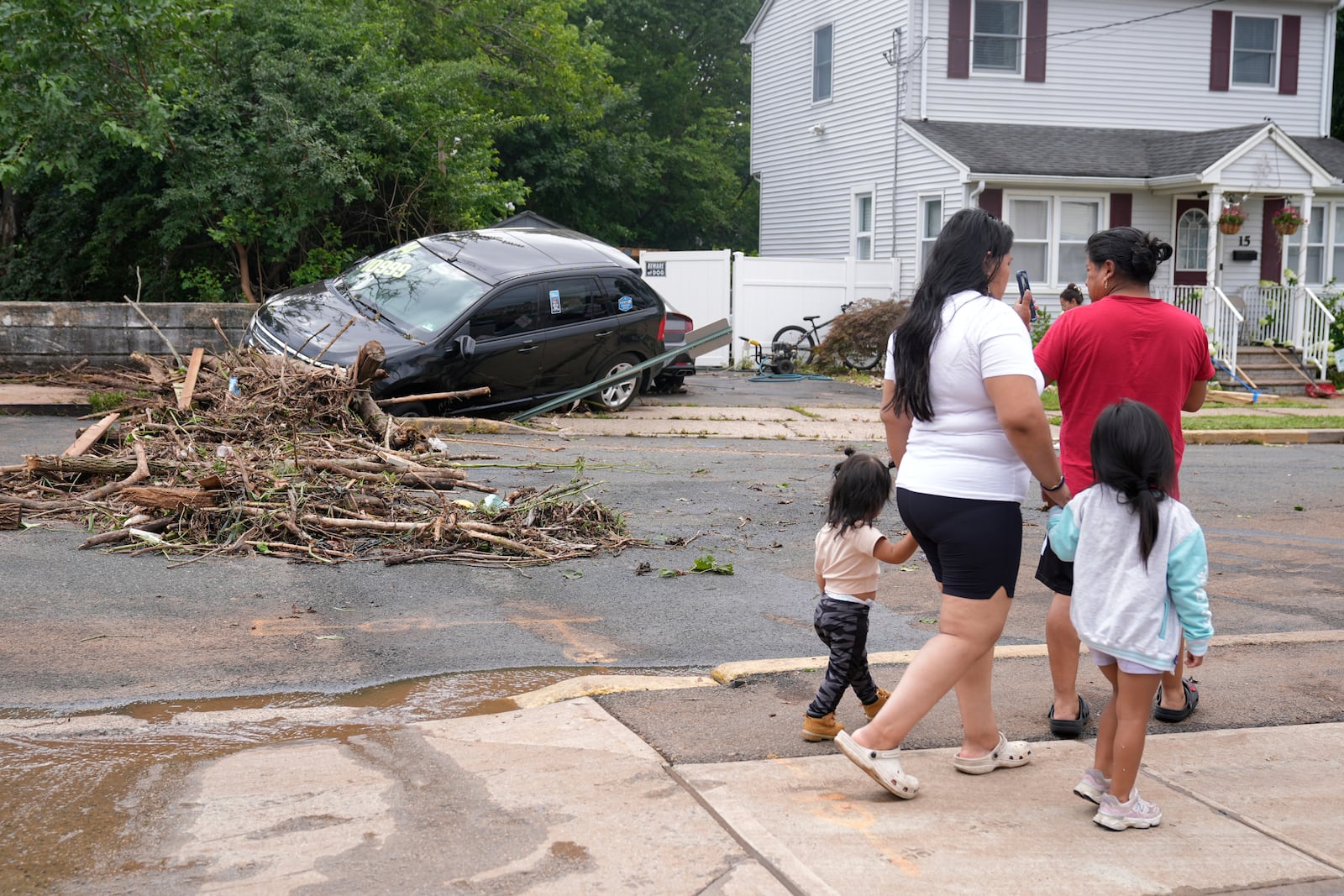 A family walks by flood-damaged cars in North Plainfield, N.J., Tuesday, July 15, 2025. (AP Photo/Seth Wenig)