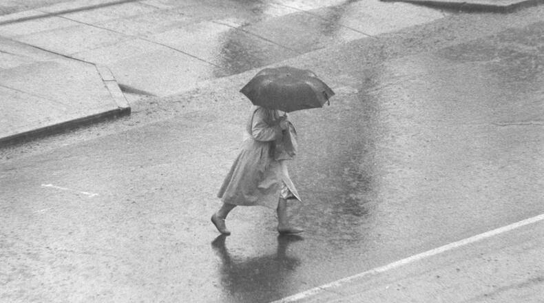 A woman walks on a rain-filled street in downtown Hamilton. Journal-News File Photo