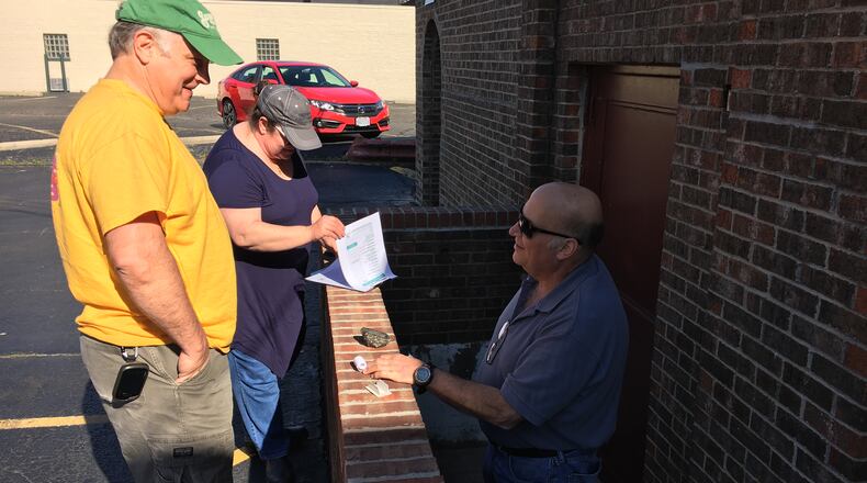 Greg Neff, of Springboro, left, helps a couple from Canada fill out their log after they found a hidden cache behind Central Pastry in Middletown. RICK McCRABB/STAFF