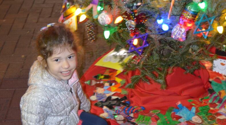 The Kiwanis Club’s decorated tree was ringed by figures of children colored by Kramer kindergarten students. Emmerson Byrd points to her art effort in the project. CONTRIBUTED/BOB RATTERMAN