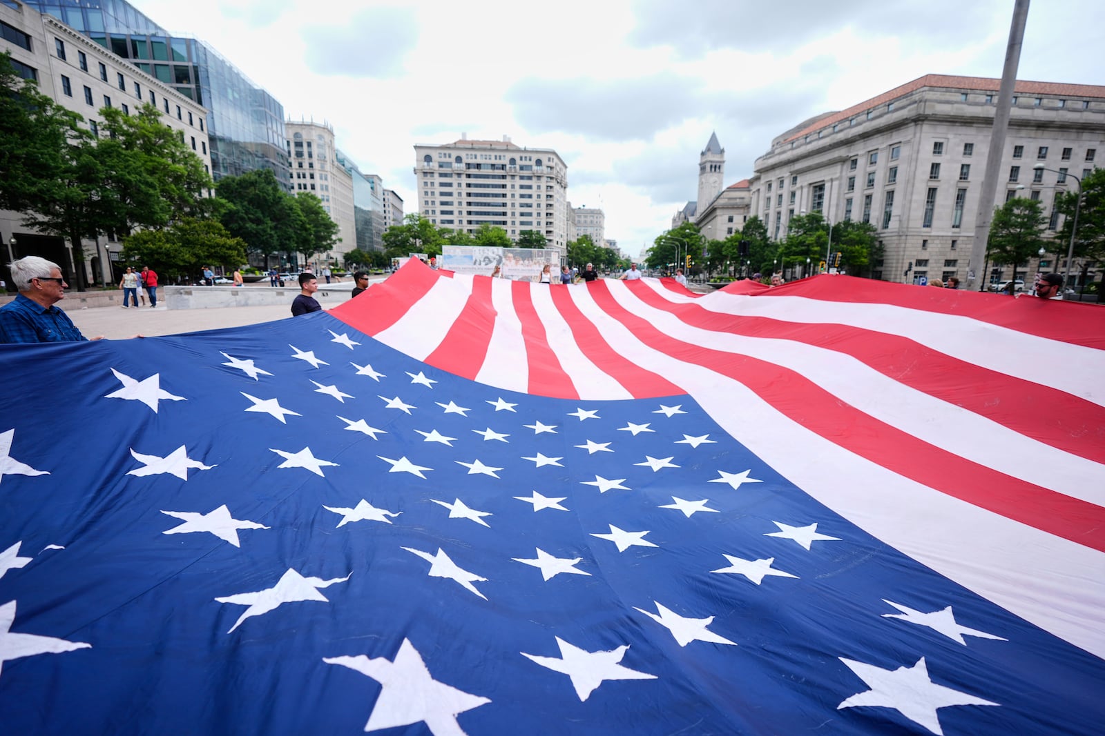 People hold a large American flag at Freedom Plaza before a parade commemorating the Army's 250th anniversary, coinciding with President Donald Trump's 79th birthday, Saturday, June 14, 2025, in Washington. (AP Photo/Manuel Balce Ceneta)