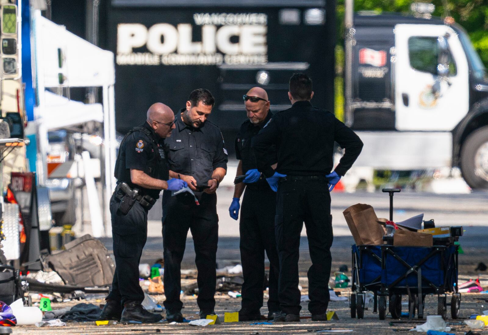Members of the Vancouver Police forensics team examine a victim's phone while investigating the scene where a vehicle drove into a crowd Saturday killing multiple people at a street festival, in Vancouver, British Columbia, Sunday, April 27, 2025. (Rich Lam/The Canadian Press via AP)
