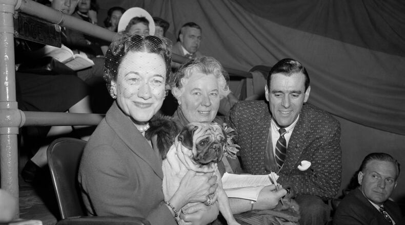 FILE - The Duchess of Windsor, Wallis Simpson, left, holds Ch. Pugville's Golden Victory during judging of the pug class during the Westminster Kennel Club Show at Madison Square Garden in New York, Feb. 13, 1956, as the dog's owner, Arnold Canton, far right, and dog breeder Harriet Smith, look on. (AP Photo/Jacob Harris, File)