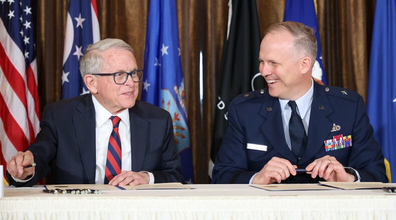 Gov. Mike DeWine (left) and Air Force Brig. Gen. Jason Bartolomei, commander of the Air Force Research Laboratory at Wright-Patterson Air Force Base, laugh while signing copies of a memorandum of understanding between the State of Ohio and AFRL on Monday at Pentagon Tower in Beavercreek. The memorandum renews a partnership between the two entities to share science and technology information and foster economic developing within Ohio. BRYANT BILLING / STAFF