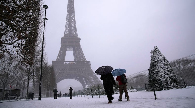 People walk near the Eiffel Tower during a snowfall Wednesday, Jan. 7, 2026 in Paris. (AP Photo/Christophe Ena)
