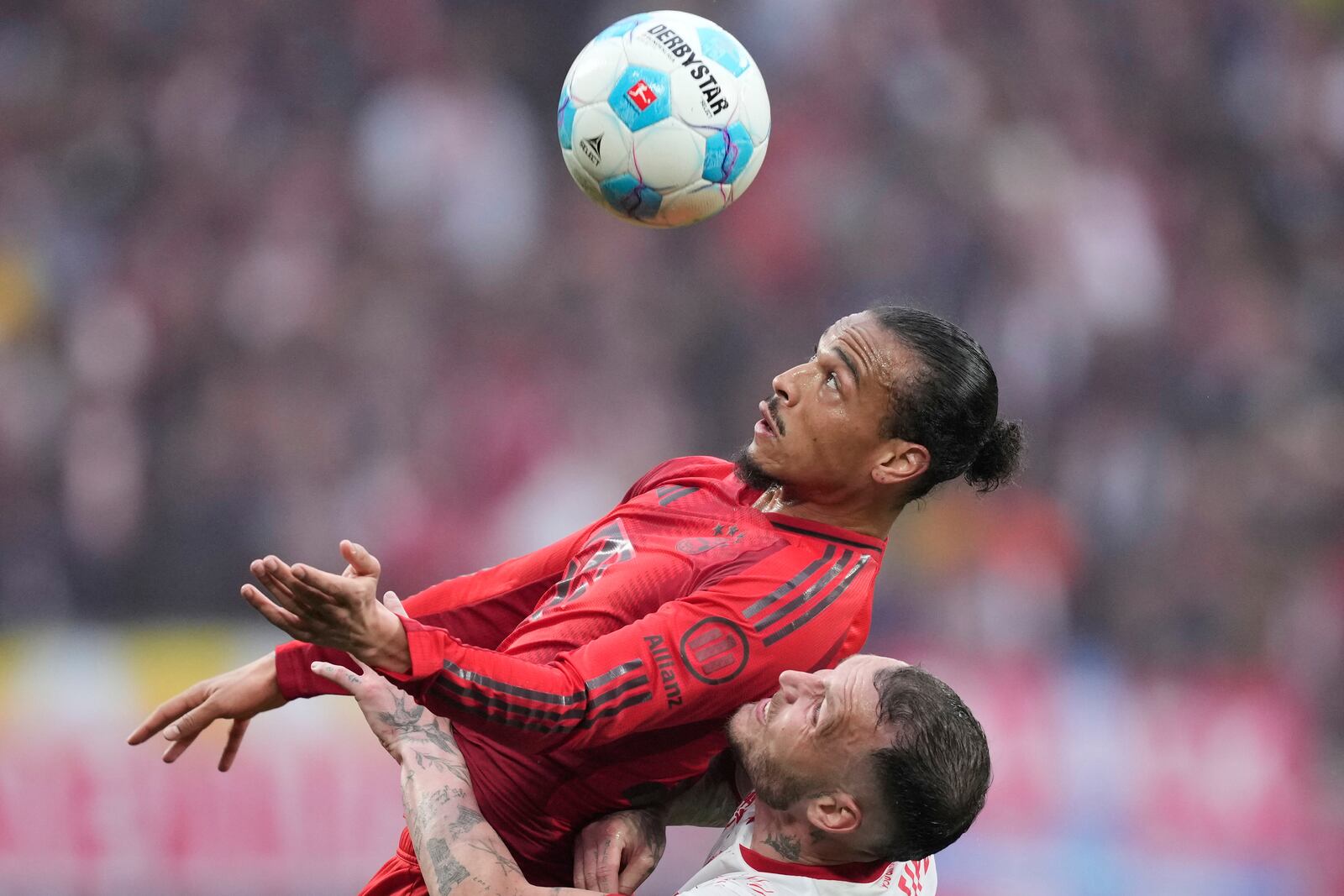 Bayern's Leroy Sane challenges for the ball with Leipzig's David Raum, bottom, during the German Bundesliga soccer match between RB Leipzig and FC Bayern Munich at the Red Bull Arena in Leipzig, Germany, Saturday, May 3, 2025. (AP Photo/Ebrahim Noroozi)