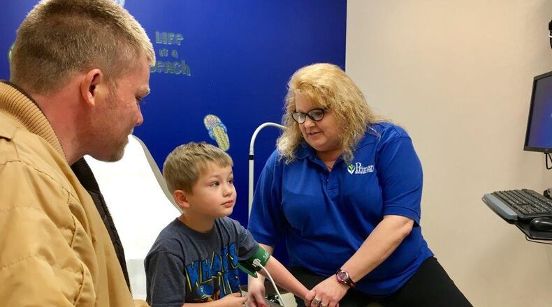 Brian Rose watches as Primary Health Solutions Clinic Medical Assistant Julie Smith treats his son Tuesday during school hours. The in-school clinic at Hamilton’s Garfield Middle School is a first for the Butler County school system.
