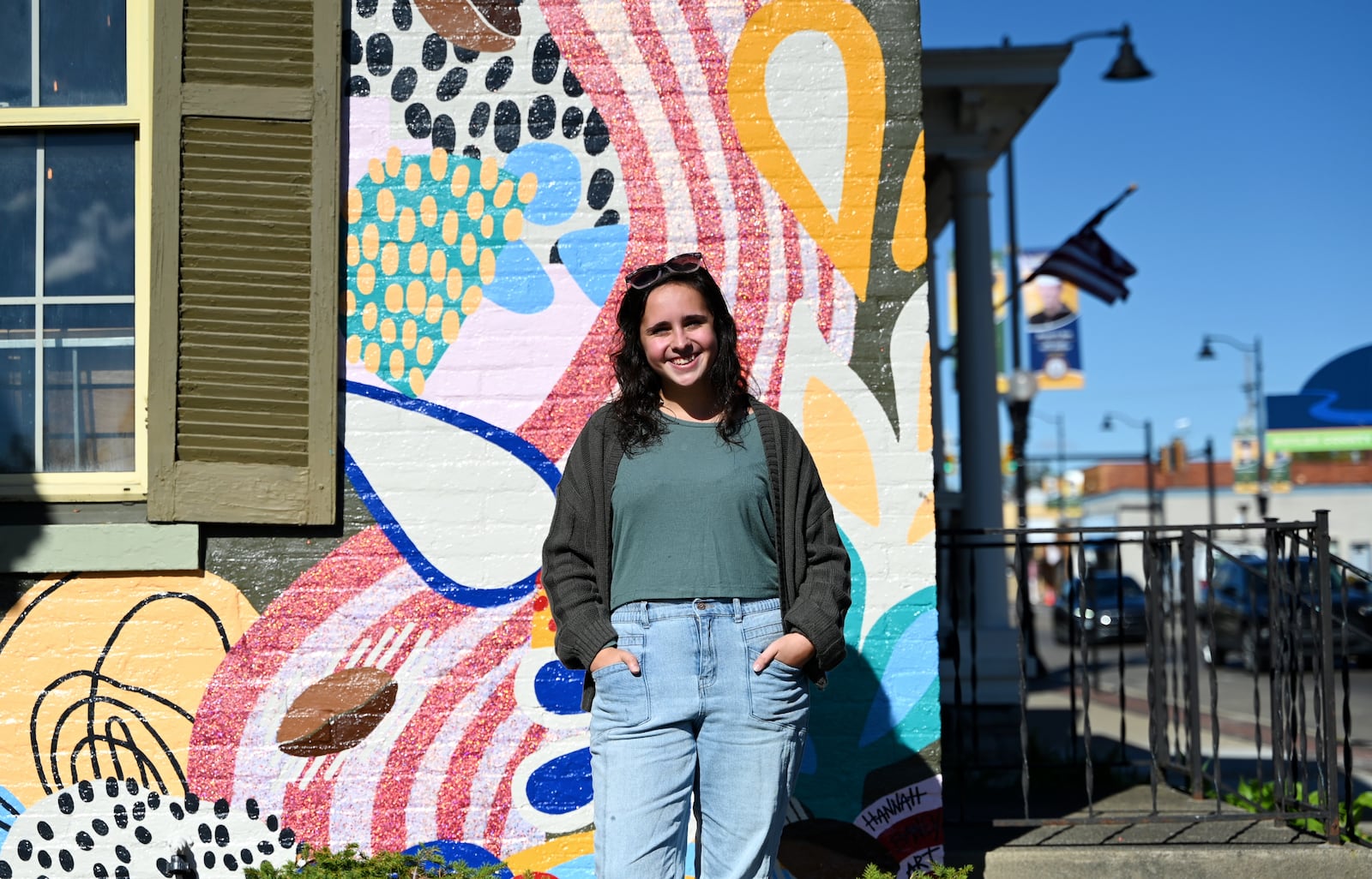 Hannah Baney, a 21-year-old art student at Miami University Hamilton, painted a mural on the east side of True West Coffee on Main Street. This mural, which she offered to do for free, landed her several paying jobs, including in her hometown in Trenton and in Hamilton. Pictured is Baney on Thursday morning, Oct. 23, 2025, in front of her mural. MICHAEL D. PITMAN/STAFF