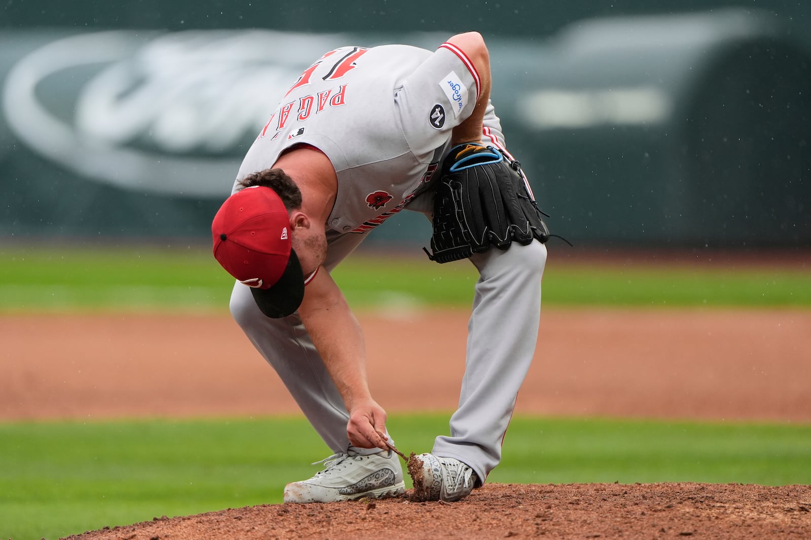 Cincinnati Reds relief pitcher Emilio Pagan scrapes mud off his shoes during the ninth inning of a baseball game against the Kansas City Royals, Monday, May 26, 2025, in Kansas City, Mo. (AP Photo/Charlie Riedel)