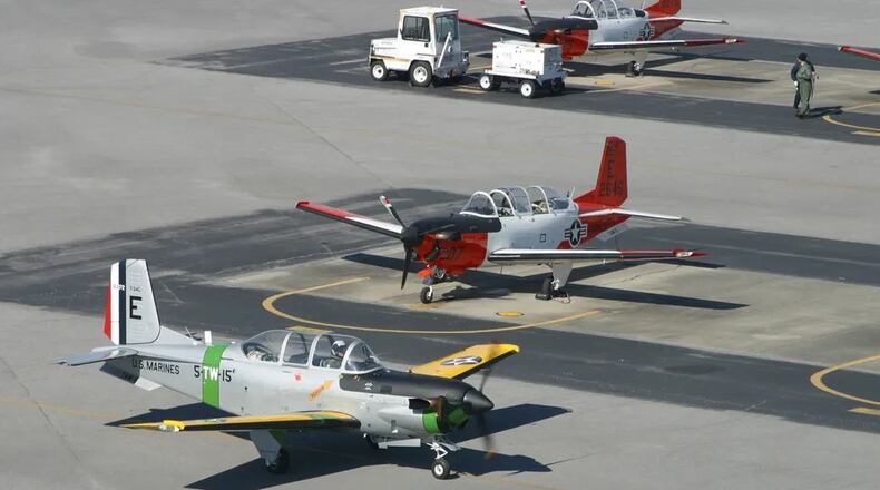 A unique T-34 "Turbo Mentor" passes in front of several other T-34's painted in orange and white colors. The aircraft's grey and yellow paint scheme, with Marine markings, were part of the Centennial of Naval Aviation's 2011 celebration. (Photo by: 2nd Lt. Molly LeBlanc)