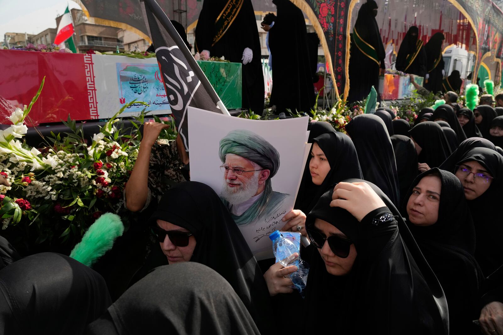 Mourners gather around the flag-draped coffins of the Iranian armed forces generals, nuclear scientists and their family members who were killed in Israeli strikes, during their funeral ceremony as one of them holds a poster of the Supreme Leader Ayatollah Ali Khamenei, in Tehran, Iran, Saturday, June 28, 2025. (AP Photo/Vahid Salemi)