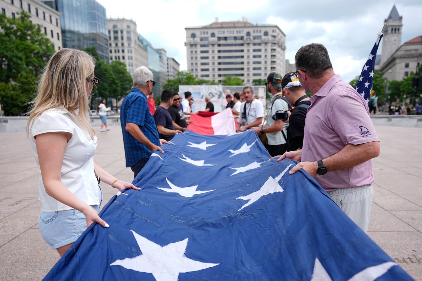 People fold a large American flag at Freedom Plaza before a parade commemorating the Army's 250th anniversary, coinciding with President Donald Trump's 79th birthday, Saturday, June 14, 2025, in Washington. (AP Photo/Manuel Balce Ceneta)
