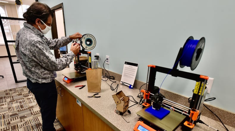A staff member feeds material to start a project on a 3D printer Tuesday at the Lane Library Community Technology Center in downtown Hamilton. NICK GRAHAM/STAFF