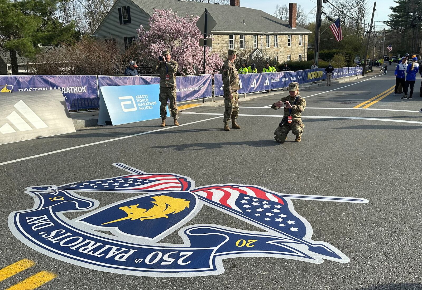 Massachusetts Army National Guard Cadet Meghan Drysdale kneels to take a photo of the road painted in commemoration of the 250th anniversary of Patriots' Day at the start of the Boston Marathon Monday, April 21, 2025. (AP Photo Jennifer McDermott)
