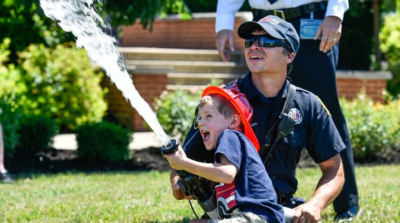 West Chester firefighter Jason Mesman helps Ascher Ruble, 4, spray the fire hose during West Chester Township's Touch A Truck event Friday, June 15 at The Square @ Union Centre. Fire trucks, police vehicles, helicopters, lift trucks, snow plows and more were on display for kids to climb in and honk horns during the free event. NICK GRAHAM/STAFF