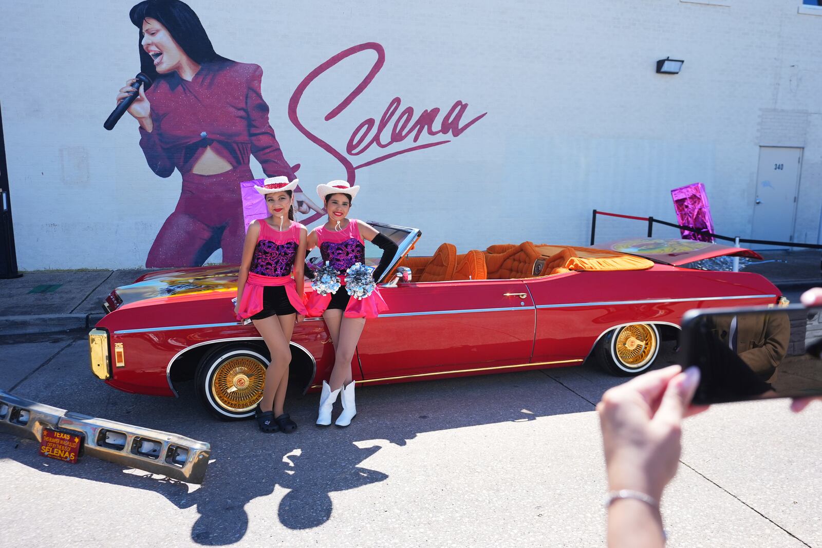 Eleven-year-olds Kataleah Mendez, right, and Angelica Juarez pose for a photo with the low rider car that appeared in the movie Selena parked for display during a Cinco de Mayo celebration in the Oak Cliff section of Dallas, Saturday, May 3, 2025. (AP Photo/LM Otero)