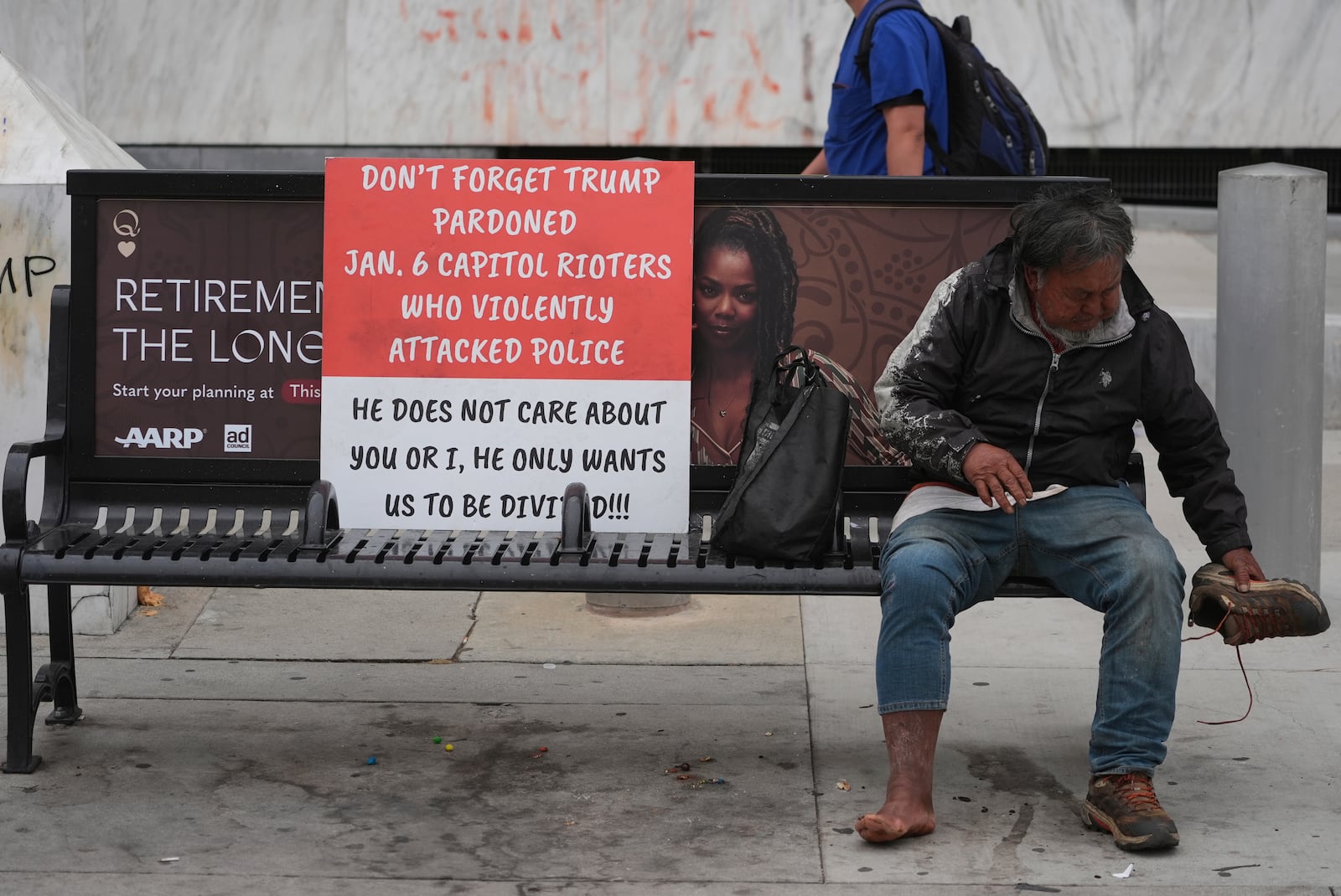 A man sits on a bench next to a poster left from recent protests against federal immigration raids, Wednesday, June 11, 2025, in Los Angeles. (AP Photo/Damian Dovarganes)
