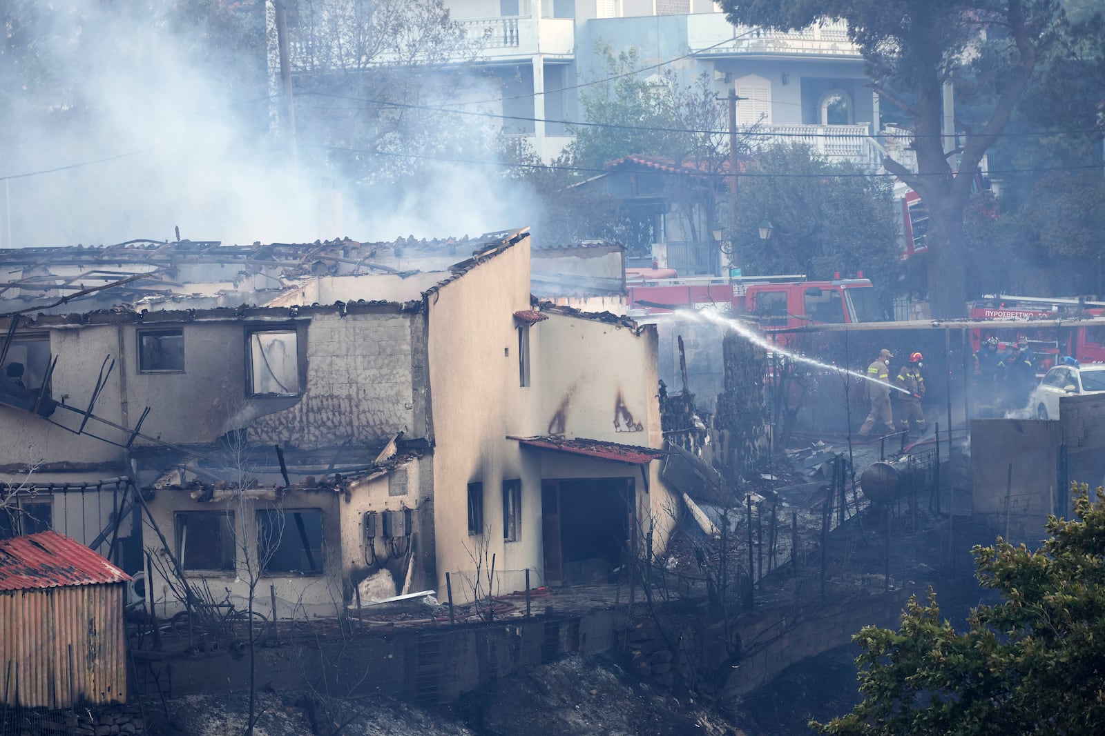 Firefighters try to extinguish a fire at a house during a wildfire, in the northwestern suburb of Kryoneri, in Athens, Greece, Saturday, July 26, 2025. (AP Photo/Yorgos Karahalis)