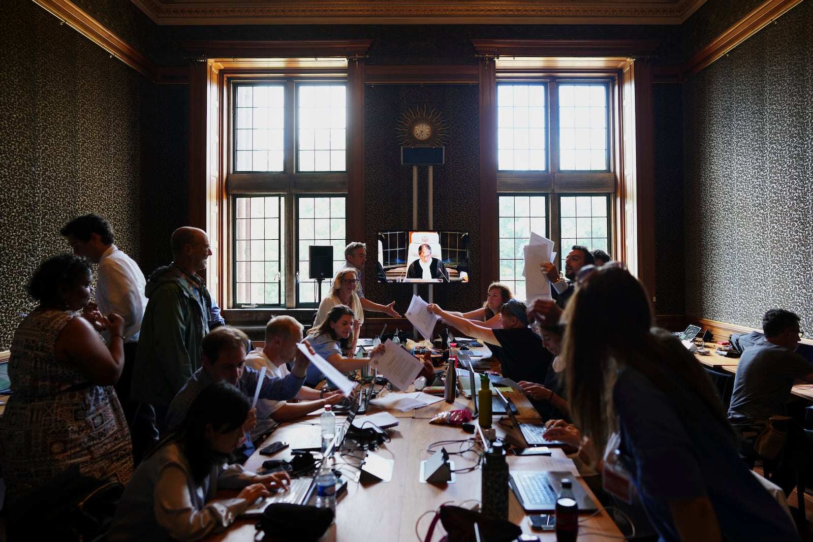 Journalists scramble to get a copy of the readings as Presiding judge Yuji Iwasawa can be seen speaking onscreen at the International Court of Justice for an advisory opinion on what legal obligations nations have to address climate change and what consequences they may face if they don't, Wednesday, July 23, 2025, in The Hague, Netherlands. (AP Photo/Peter Dejong)