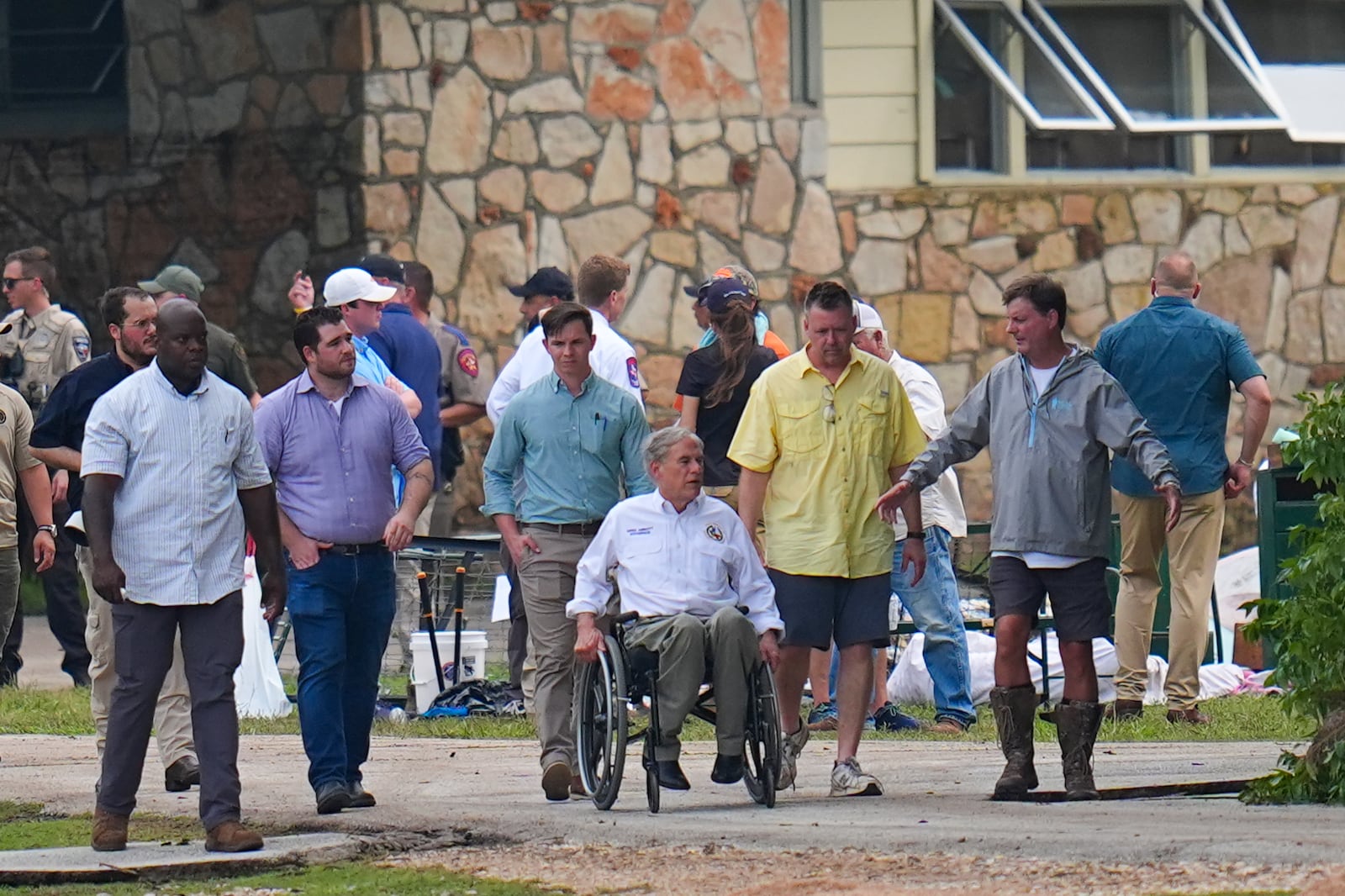 Texas Gov. Greg Abbott, center, tours Camp Mystic along the banks of the Guadalupe River after a flash flood swept through the area Saturday, July 5, 2025, in Hunt, Texas. (AP Photo/Julio Cortez)