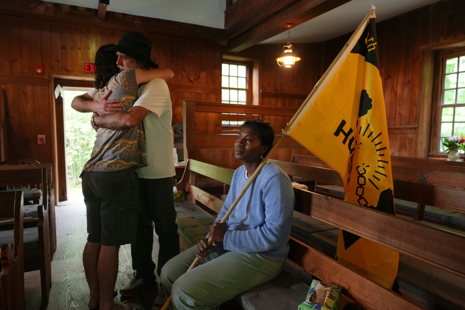 Casey Oware, a member of the Princeton Friends Meeting, seated, holds a flag while Stuart Sydenstricker, right, and Jules Wing Vasquez hug after completing a portion of the Quaker March to Washington at the Quaker Meeting House in Princeton, N.J. (AP Photo/Luis Andres Henao)