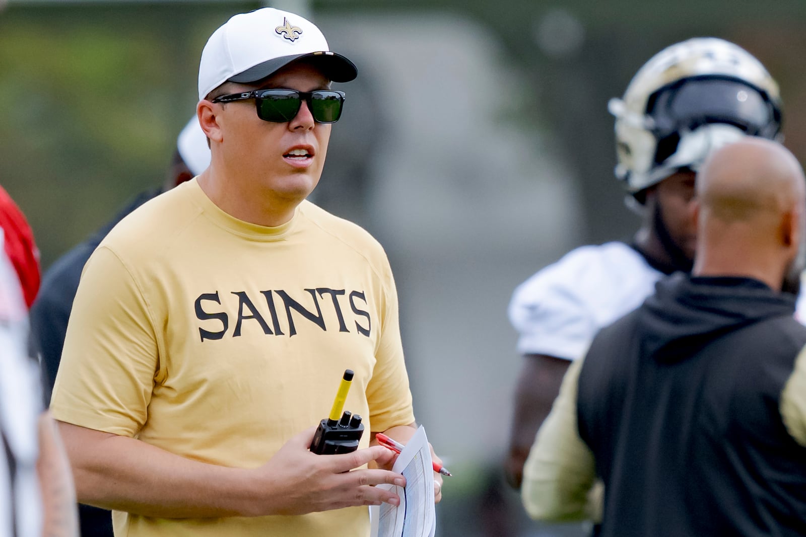 New Orleans Saints head coach Kellen Moore carries a walkie talkie during the team's NFL football training camp in Metairie, La., Wednesday, July 23, 2025. (AP Photo/Matthew Hinton)