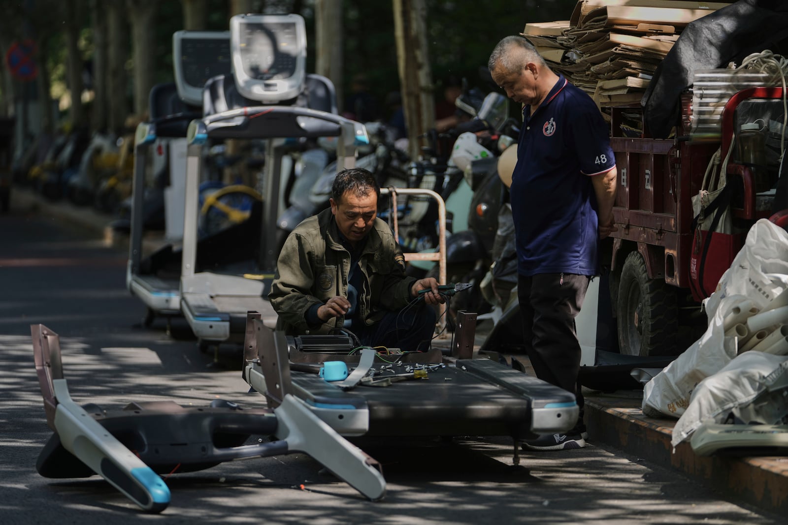 Workers dismantle unwanted gym treadmill machine parts for sale with junks along a street in Beijing, Monday, April 28, 2025. (AP Photo/Andy Wong)