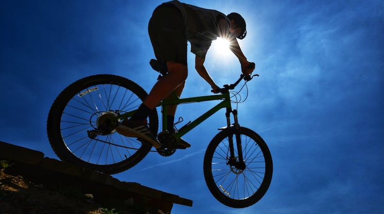 Reece Jackson, from Morrow, rides his bike on the jump line silhouetted in the sun at Premier Health Atrium Medical Center Bike Park Monday, July 1 in Lebanon. NICK GRAHAM/STAFF