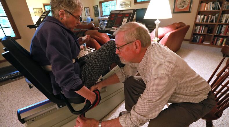 Steve Sidlo helps his wife, Cynthia, get into position on her exercise bike Wednesday in their Springfield home. Cynthia is recovering from a stroke several years ago. BILL LACKEY/STAFF