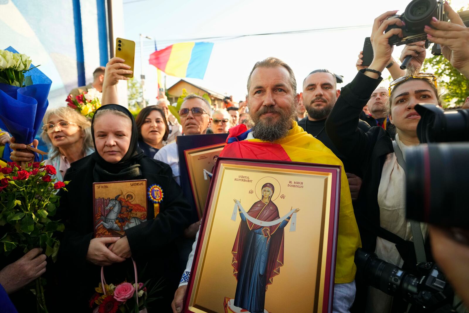 Supporters hold religious icons outside the voting station where Calin Georgescu, winner of the first round of last year's annulled election, and Presidential candidate George Simion voted in the first round of the presidential election redo in Bucharest, Romania, Sunday, May 4, 2025. (AP Photo/Vadim Ghirda)