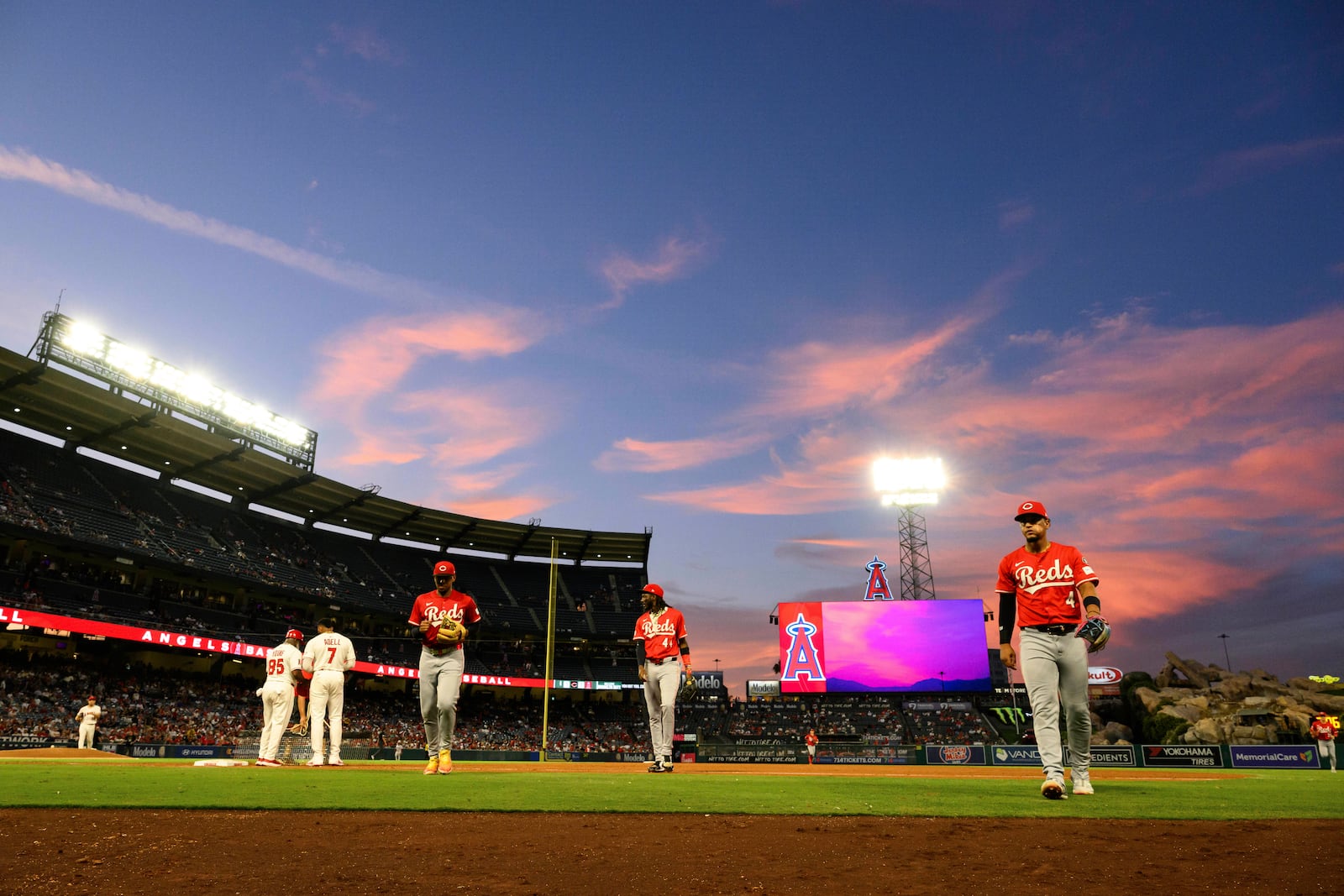 Cincinnati Reds players walk back to the dugout during sunset in the fourth inning of a baseball game against the Los Angeles Angels, Wednesday, Aug. 20, 2025, in Anaheim, Calif. (AP Photo/William Liang)