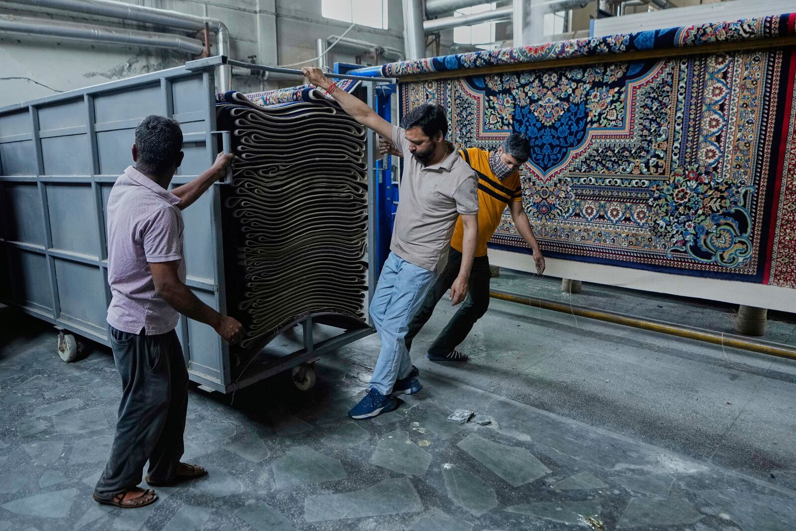 Indian workers push a cart loaded with carpets at a factory on the outskirts of Jammu, India, Tuesday, April 8, 2025. (AP Photo/Channi Anand)