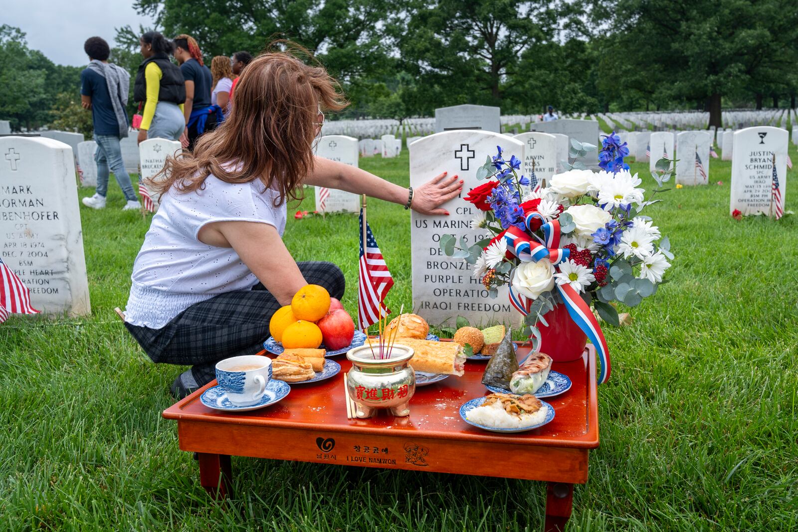 FILE - Kim Hoan Nguyen, of Falls Church, Va., who is originally from Vietnam, touches her son's gravestone next to ritual offerings in the Vietnamese tradition at the gravesite of her son, Marine Corporal Binh N Le, who died serving in Iraq in 2004, in Section 60 of Arlington National Cemetery, in Arlington, Va., Monday, May 27, 2024, on Memorial Day. (AP Photo/Jacquelyn Martin, File)