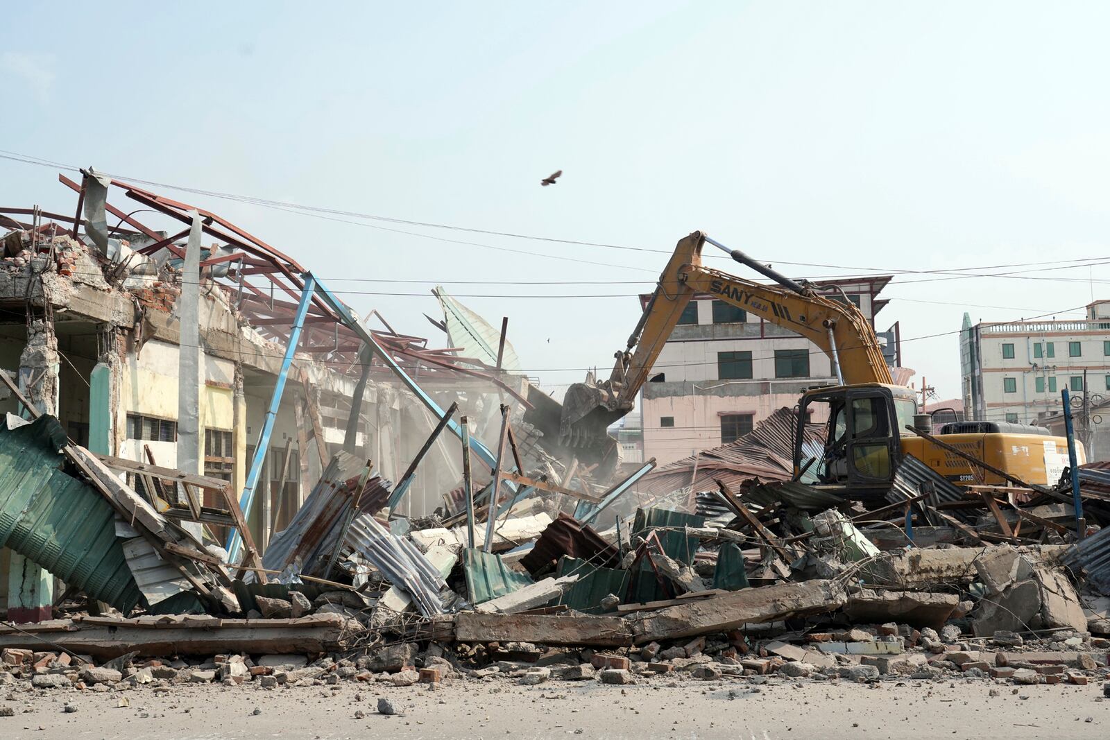 A volunteer drives a backhoe to clear debris of a building at a market, after one month of the strong earthquake in Naypyitaw, Myanmar, Monday, April 28, 2025. (AP Photo/Aung Shine Oo)