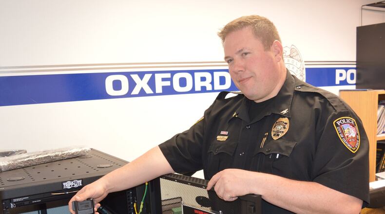 Police Chief John Jones holds one of the department s body worn cameras on top of the docking station which charges the units and also serves as a computer link for downloading the video. CONTRIBUTED/BOB RATTERMAN