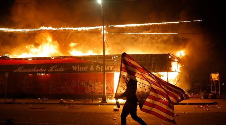 A protester carries a U.S. flag upside, a sign of distress, next to a burning building Thursday, May 28, 2020, in Minneapolis. Protests over the death of George Floyd, a black man who died in police custody Monday, broke out in Minneapolis for a third straight night. (AP Photo/Julio Cortez)