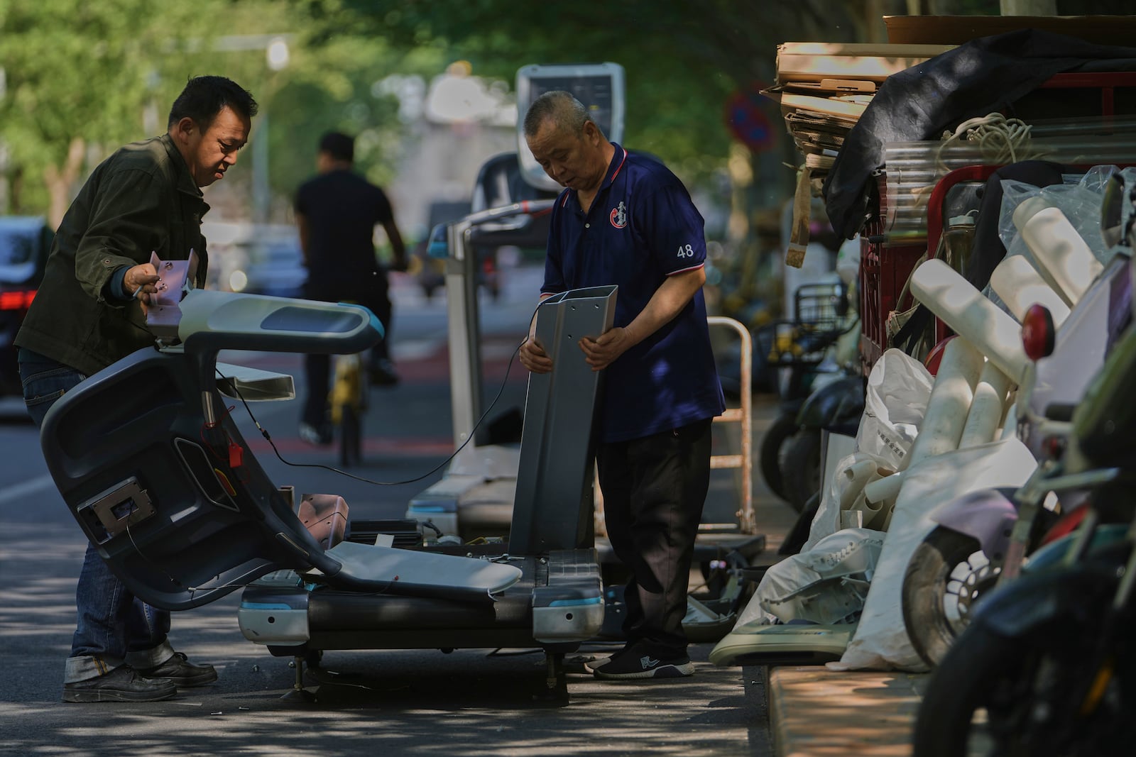 Workers dismantle unwanted gym treadmill machine parts for sale with junks along a street in Beijing, Monday, April 28, 2025. (AP Photo/Andy Wong)