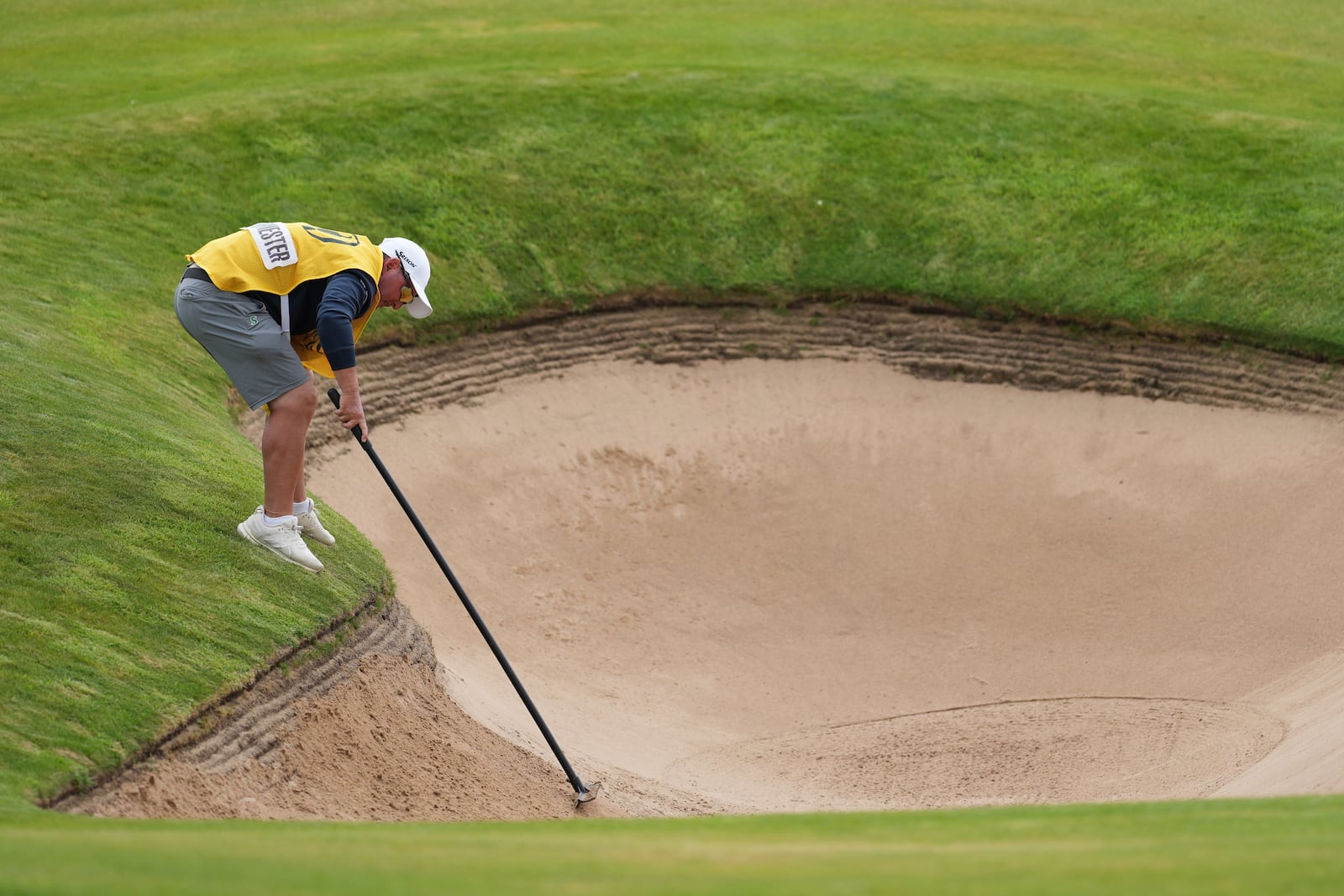 Jason Reynolds caddie for Dean Burmester of South Africa of South Africa, rakes a bunker on the 1st after Burmester played a shot from it during the third round of the British Open golf championship at the Royal Portrush Golf Club, Northern Ireland, Saturday, July 19, 2025. (AP Photo/Jon Super)