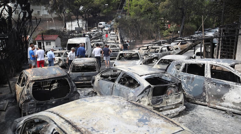 FILE - People stand amid the charred remains of burned-out cars in Mati east of Athens, Tuesday, July 24, 2018. (AP Photo/Thanassis Stavrakis, File)