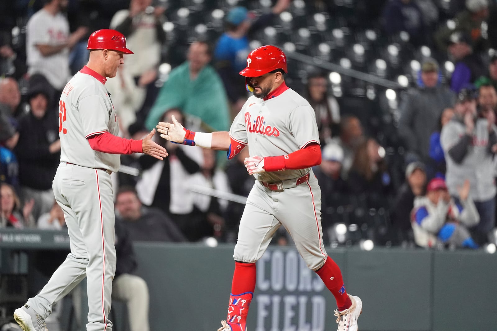 Philadelphia Phillies third base coach Dusty Wathan, left, congratulates Kyle Schwarber, right, who circles the bases after hitting a solo home run off Colorado Rockies relief pitcher Scott Alexander in the ninth inning of a baseball game Monday, May 19, 2025, in Denver. (AP Photo/David Zalubowski)