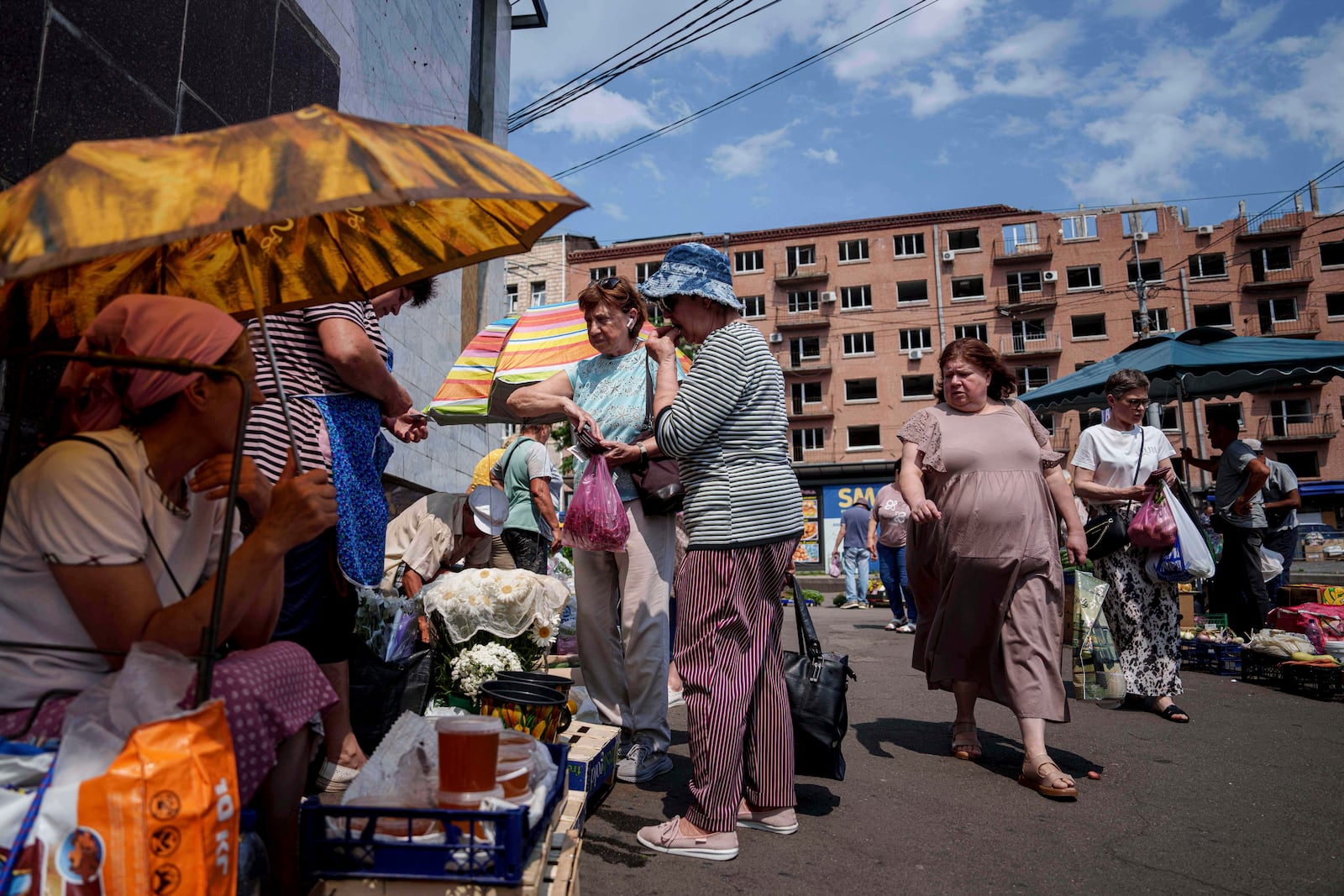 People shop at a street market near a building which was damaged by a Russian attack in Kyiv, Ukraine, on Thursday, July 10, 2025. (AP Photo/Evgeniy Maloletka)