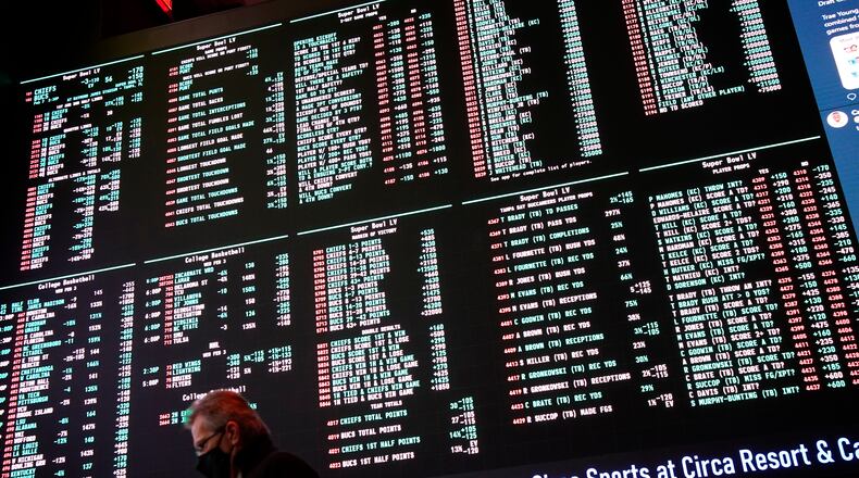A man walks by as betting odds for NFL football's Super Bowl 55 are displayed on monitors at the Circa resort and casino sports book, Wednesday, Feb. 3, 2021, in Las Vegas. (AP Photo/John Locher)