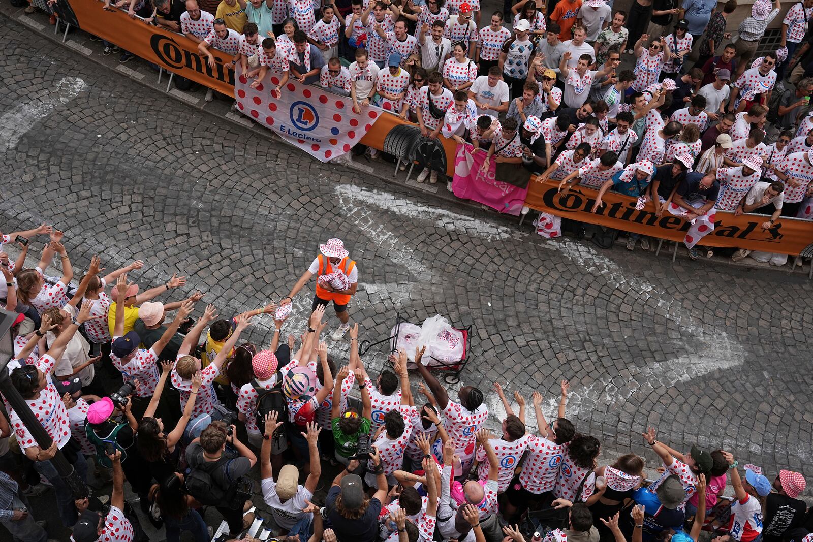 A man distributes publicity items to cycling fans in a packed street of the Montmartre district during the last stage of the Tour de France cycling race between Mantes-la-Ville and Paris, Sunday, July 27, 2025 in Paris (AP Photo/Laurent Cipriani)