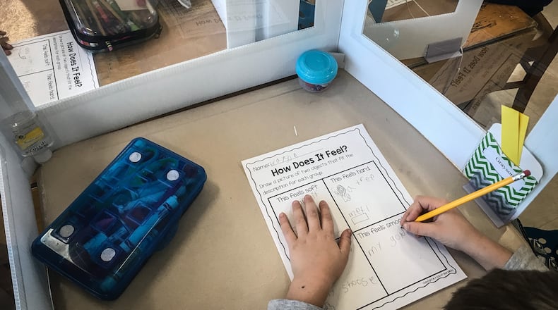 First-grade students at Kettering's Orchard Park Elementary School do their work with protective plastic around their desks Tuesday, March 2, 2021. STAFF / JIM NOELKER